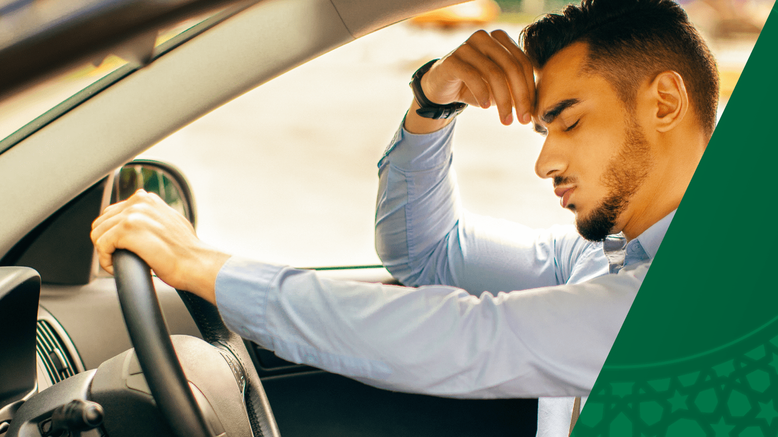 A man is seated in the driver seat of his car. He looks sad with his hand across it forehead while he leans forward